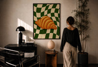Croissant on Green Checkerboard print in a black frame on a sunlit plaster wall, a woman looking on beside a mushroom lamp