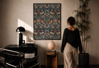 William Morris Strawberry Thief print in a black frame on a sunlit plaster wall, a woman looking on beside a mushroom lamp