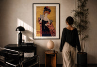 Cappiello Hélène Chauvin print in a black frame on a sunlit plaster wall, a woman looking on beside a mushroom lamp