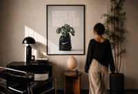 Nike x Monstera Garbage Bag print in a black frame on a sunlit plaster wall, a person looking on beside a mushroom lamp