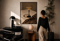 Champagne Coupe with Leopard Print in a black frame on a sunlit plaster wall, a person looking on beside a mushroom lamp
