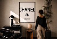 Coco Chanel Quote Typography print in a black frame on a sunlit plaster wall, a person looking on beside a mushroom lamp