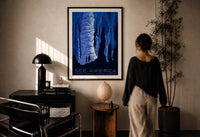 WPA See America Caverns print in a black frame on a sunlit plaster wall, a woman looking on beside a mushroom lamp
