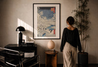 Hiroshige Meguro Bridge in Snow print in a black frame on a sunlit plaster wall, a woman looking on beside a mushroom lamp