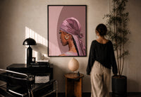 Black Woman in a Pink Durag print in a black frame on a sunlit plaster wall, a woman looking on beside a mushroom lamp