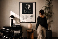 Drake Scorpion Album Tracklist print in a black frame on a sunlit plaster wall, a person looking on beside a mushroom lamp