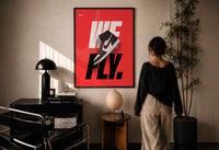 Nike Air Jordan 1 We Fly print in a black frame on a sunlit plaster wall, a person looking on beside a mushroom lamp