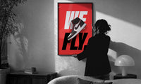 Nike Air Jordan 1 We Fly print in a slim black frame being hung on a sunlit wall in a monochrome room