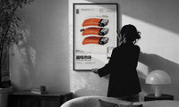 SEAxFOOD Market Salmon Sushi Lighter print in a slim black frame being hung on a sunlit wall in a monochrome room