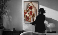 Figs, Cheese and Walnuts print in a slim black frame being hung on a sunlit wall in a monochrome room