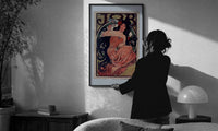 Mucha JOB print in a slim black frame being hung on a sunlit wall in a monochrome room