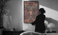 William Morris Honeysuckle print in a slim black frame being hung on a sunlit wall in a monochrome room
