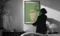 Just Do It Chameleon Green Pink print in a slim black frame being hung on a sunlit wall in a monochrome room