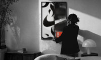 Nike Swoosh Streetwear print in a slim black frame being hung on a sunlit wall in a monochrome room