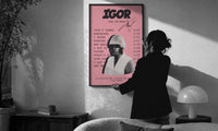Pink Tyler, the Creator IGOR Tracklist print in a slim black frame being hung on a sunlit wall in a monochrome room