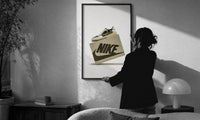 Air Jordan 1 Travis Scott Olive Sneaker print in a slim black frame being hung on a sunlit wall in a monochrome room