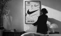 Nike Swoosh Black and White Typography print in a slim black frame being hung on a sunlit wall in a monochrome room