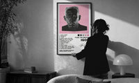 Tyler, The Creator IGOR Tracklist print in a slim black frame being hung on a sunlit wall in a monochrome room