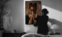Black Woman with Clasped Hands print in a slim black frame being hung on a sunlit wall in a monochrome room