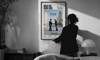 Pink Floyd Wish You Were Here Burning Handshake print in a slim black frame being hung on a sunlit wall in a monochrome room