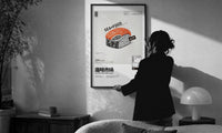 SEAxFOOD Market Original Salmon Sushi print in a slim black frame being hung on a sunlit wall in a monochrome room