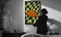 Croissant on Green Checkerboard print in a slim black frame being hung on a sunlit wall in a monochrome room