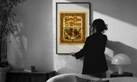 Thomas Nast Santa Claus Works Cover print in a slim black frame being hung on a sunlit wall in a monochrome room