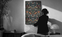William Morris Strawberry Thief print in a slim black frame being hung on a sunlit wall in a monochrome room