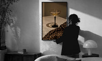 Champagne Coupe with Leopard Print in a slim black frame being hung on a sunlit wall in a monochrome room