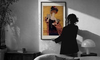 Cappiello Hélène Chauvin print in a slim black frame being hung on a sunlit wall in a monochrome room
