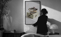 Air Jordan 1 Travis Scott Reverse Mocha print in a slim black frame being hung on a sunlit wall in a monochrome room