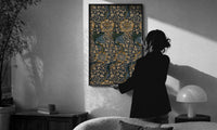 William Morris Kennet print in a slim black frame being hung on a sunlit wall in a monochrome room