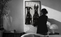 Doberman Pinscher Portrait Duo print in a slim black frame being hung on a sunlit wall in a monochrome room