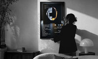 Daft Punk Random Access Memories Helmets print in a slim black frame being hung on a sunlit wall in a monochrome room