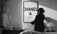 Coco Chanel Quote Typography print in a slim black frame being hung on a sunlit wall in a monochrome room