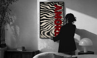 Amore Zebra Print in a slim black frame being hung on a sunlit wall in a monochrome room