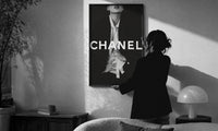 Chanel Black & White Luxury print in a slim black frame being hung on a sunlit wall in a monochrome room