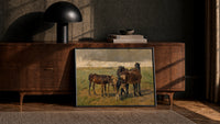 Group of horses in field print in a black frame leaning against a walnut console in lamplight