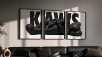 KAWS Monochrome Family Poster Set of 3 in black frames on a grey wall above a leather sofa