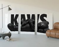 KAWS Monochrome Family Poster Set of 3 displayed beside a brown leather sofa