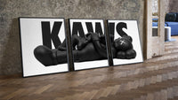 KAWS Monochrome Family Poster Set of 3 leaning on parquet beside a vintage loft door