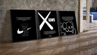 KAWS Monochrome Wall Art Set three-piece set leaning on parquet beside a vintage loft door