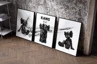 KAWS x Nike Blackout Poster Set of 3 as black-framed prints leaning against a raw-plaster wall