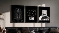 KAWS Monochrome Statement triptych in three black frames on a grey wall above a leather sofa