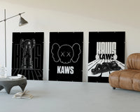 KAWS Monochrome Statement three-panel set displayed beside a brown leather sofa