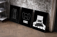 KAWS Monochrome Statement set of three black-framed prints leaning against a raw-plaster wall