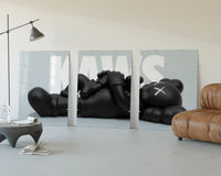 KAWS Reclining Companion Triptych displayed beside a brown leather sofa