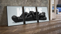 KAWS Reclining Companion Triptych leaning on parquet beside a vintage loft door