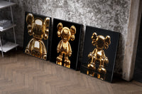 KAWS 24K Gold Figure Art Print Set of 3 as black-framed prints leaning against a raw-plaster wall
