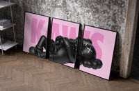 KAWS Pink Reclining Companion Set of 3 as black-framed prints leaning against a raw-plaster wall